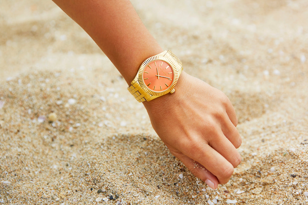 Reloj dorado para mujer con esfera de color coral.