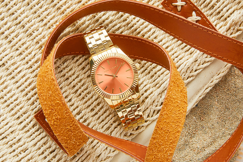 Reloj dorado para mujer con esfera de color coral.